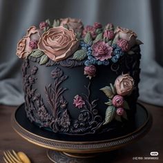 there is a black cake with pink and blue flowers on the top, along with gold forks