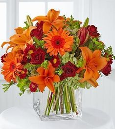 a vase filled with orange and red flowers on top of a white table next to a window