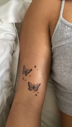 a woman's arm with two butterflies on it and stars in the sky above her