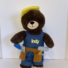 a brown teddy bear wearing blue overalls holding tools