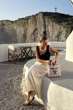 a woman sitting on top of a stone wall next to a bag and purse in her hand