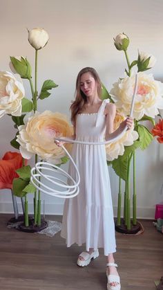 a woman in a white dress standing next to large flowers and holding a stick with one hand