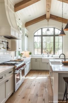 a large kitchen with white cabinets and wood flooring, along with an arched window