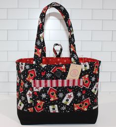 a black and red handbag with christmas decorations on the front is sitting in front of a white brick wall