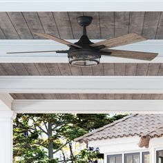 a ceiling fan mounted to the side of a white house with wood planks on it