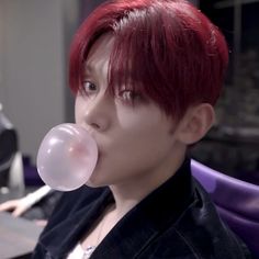 a person with red hair blowing a bubble