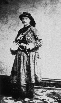 an old black and white photo of a woman standing in front of a wall wearing a hat