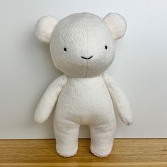 a white teddy bear sitting on top of a wooden table next to a white wall