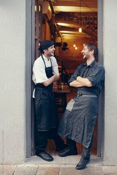 two men in aprons are standing at the door