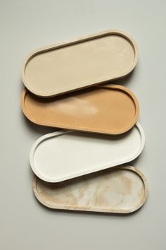 three oval trays are stacked on top of each other, one is white and the other is beige