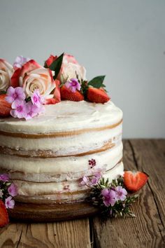 a white cake with flowers and strawberries on the top is sitting on a wooden table