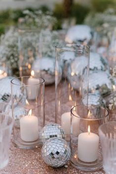 a table topped with lots of glass vases filled with white candles and disco balls