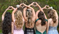 four girls in dresses are making heart shapes with their hands while standing next to each other