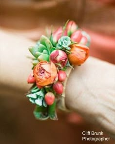 a woman's hand holding an orange flower and succulent bracelet