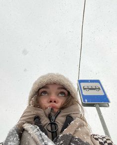 a woman standing in front of a bus stop sign covered in snow with her mouth open