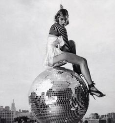 a woman sitting on top of a disco ball in front of a cityscape