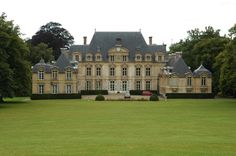 a large building with lots of windows in the middle of a grassy area next to trees