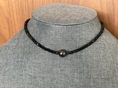 This black on black choker is a true showstopper. I've chosen one beautiful 9mm Tahitian black pearl, AAA/AA quality, and paired it with 4mm black Tourmaline faceted rondelles to make a choker that is a black lover's dream.  The Tahitian pearl is a genuine South Sea pearl imported from Tahiti and has not been dyed or colored in any way. The pearl is truly the center of attention in this piece but the inky opaque sparkling faceted black schorl Tourmaline rondelles aren't exactly wallflowers.  The pearl is very subtly set off from the opals by two tourmaline stones that, when lit from behind, show they are actually more blue green to hint at the green and blue luster in the pearl they flank.  I have a few sizing options; please measure your neck with a string and then measure the string with Black Single Strand Pearl Necklace, Formal Black Tahitian Pearl Necklaces, Black Single Strand Pearl Necklace As Gift, Black Single Strand Tahitian Pearl Necklace, Black Tahitian Pearl Single Strand Necklace, Elegant Black Choker With Round Beads, Black Single Strand Choker Necklace, Black Tahitian Pearl Single Strand Jewelry, Formal Black Necklace With Pearl Pendant