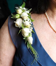 a woman wearing a blue dress holding a bouquet of white roses and greenery on her neck