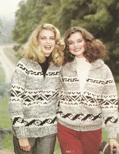 two women standing next to each other in sweaters and pants with trees in the background