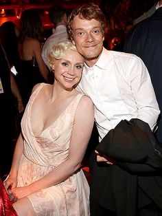 a man and woman posing for the camera at a formal event with other people in the background