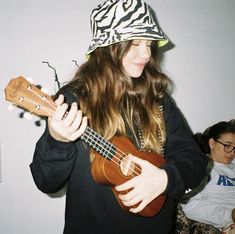 a woman with long hair wearing a zebra print hat and playing a ukulele