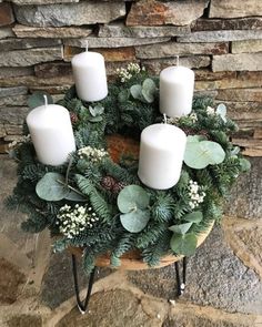 a wreath with white candles and greenery in front of a stone wall