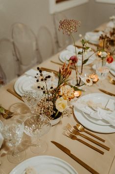 the table is set with white plates and gold cutlery, silverware, and flowers