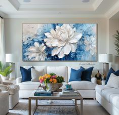 a living room filled with white couches and blue pillows in front of a large painting