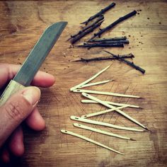 a person is holding a knife over several matches on a table with sticks and nails