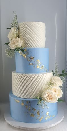 a three tiered cake with white flowers and blue icing