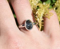 a close up of a person's hand with a ring on it and flowers in the background