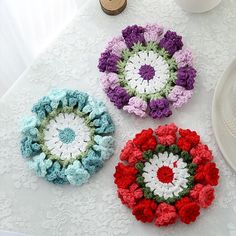 three crocheted flower coasters sitting on a table next to a white plate