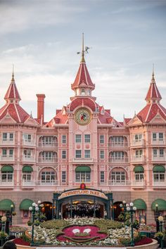 a large pink building that has a clock on it's face in front of the entrance