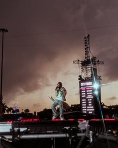 a man standing on top of a stage with a guitar in his hand and lights behind him