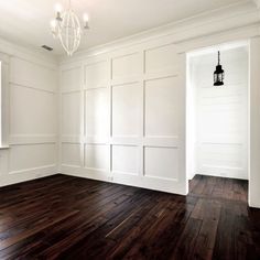 an empty room with white walls and wood floors, chandelier hanging from the ceiling