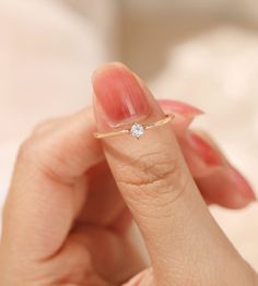 a woman's hand holding a diamond ring in her left hand, with the middle finger touching it