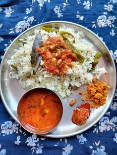 a silver plate topped with rice and beans next to a bowl of red sauce on a blue table cloth