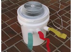 a white bucket sitting on top of a brick floor next to a fan and wires