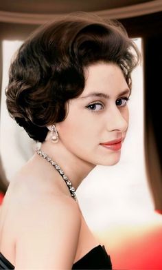 a woman with short hair wearing a black dress and diamond necklace, looking off to the side