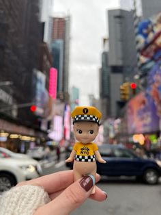 a hand holding a tiny toy in the middle of a city street