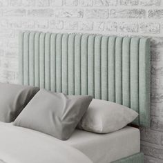 a bed with two pillows on top of it next to a brick wall and headboard