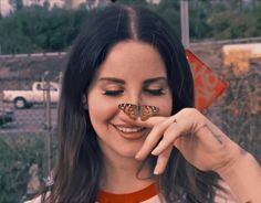 a woman is smiling and holding a butterfly in front of her face while looking at the camera