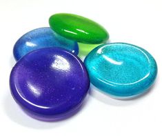 three different colored rocks sitting next to each other on a white surface with blue, green and purple speckles