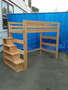 a wooden bunk bed sitting next to a blue tarp covered building with stairs leading up to it