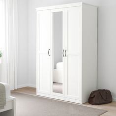 a white armoire with mirrored doors in a room next to a rug and window