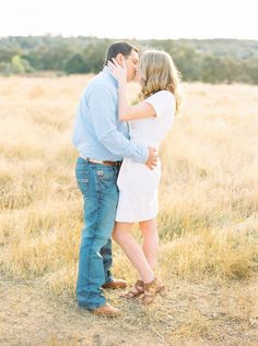 a man and woman kissing in the middle of an open field with tall dry grass