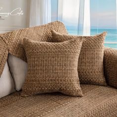 a couch with some pillows on top of it near a window and the ocean in the background