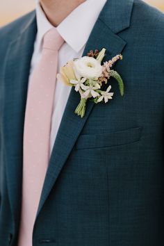 a man in a suit and tie with flowers on his lapel flower is wearing a pink tie