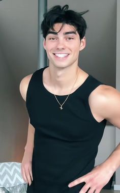 a young man wearing a black tank top smiling at the camera with his hands on his hips